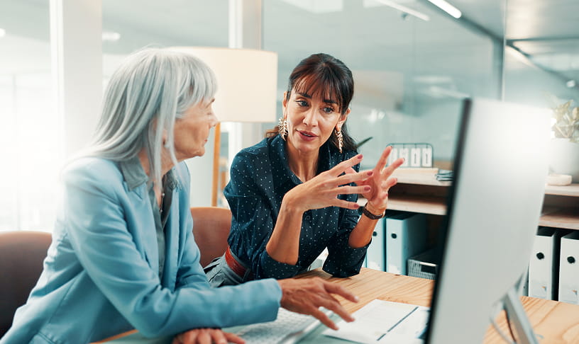 Two women discussing information on a computer screen in an office